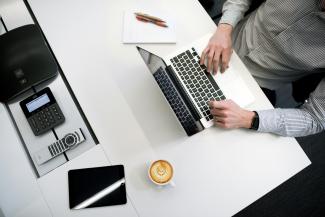 person using laptop on white wooden table by Tyler Franta courtesy of Unsplash.